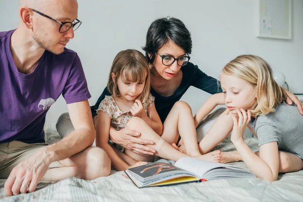 Семья сидит на кровати чтение книги вместе — стоковое фото