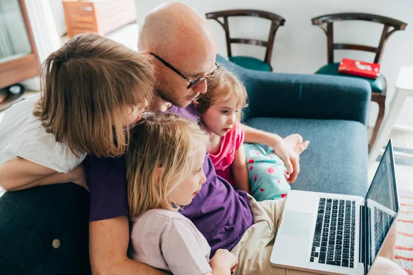 Отец смотрит потоковый фильм на компьютере с тремя дочерьми — стоковое фото