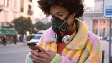 Milano 'da dışarıda poz veren genç bir kadının sağlık maskesi takıp akıllı telefon kullanarak kirlilikten ve virüsten korunması. Anti-duman, enfeksiyon, koruma konsepti.