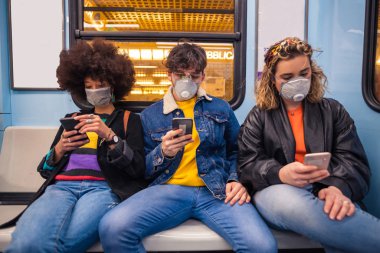 Three multiethnic friends wearing medical mask protecting from pollution and virus in the subway using smartphone - anti-smog, infection, protester concept clipart