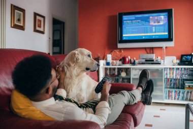 Genç yakışıklı siyah adam evde köpek gibi televizyon seyrederek kanepede oturuyor - rahat, eğlence, rahatlama konsepti