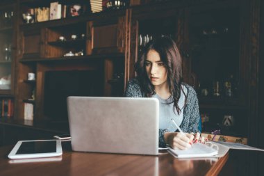 Genç, güzel, orta doğulu bir kadın evde bilgisayar kullanarak deftere not alıyor. Akıllı öğrenme, akıllı çalışma, iş önlemi.