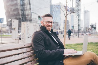 Genç, yakışıklı, beyaz, zeki bir adam bilgisayar tebessümü kullanarak bankta oturuyor. Serbest çalışan, iş adamı, 5G teknolojili konsept.