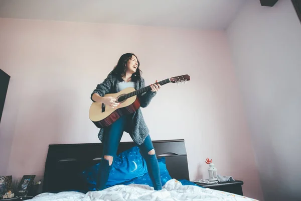 若い美しい中東の女性屋内で自宅のベッドルームでギタージャンプベッドをプレイ 感情的 インスピレーション 遊び心のあるコンセプト — ストック写真