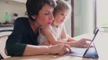 Yetişkin kadın anne, kadın çocuğa tablet bilgisayar, ebeveyn kontrolü ve öğretim konsepti kullanarak ders veriyor.