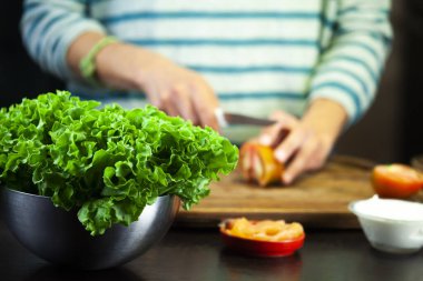 Kız tahta kesme tahtasıyla domatesi kesiyor.