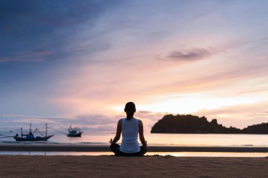 Gün batımında plajda yoga yapan genç bir kadın..