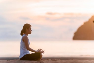 Gün doğumunda sahilde yoga yapan genç bir kadın..