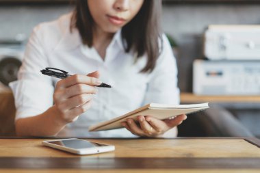 Bir kahve fincanı ve defter ile akıllı telefon kullanan genç kadın.