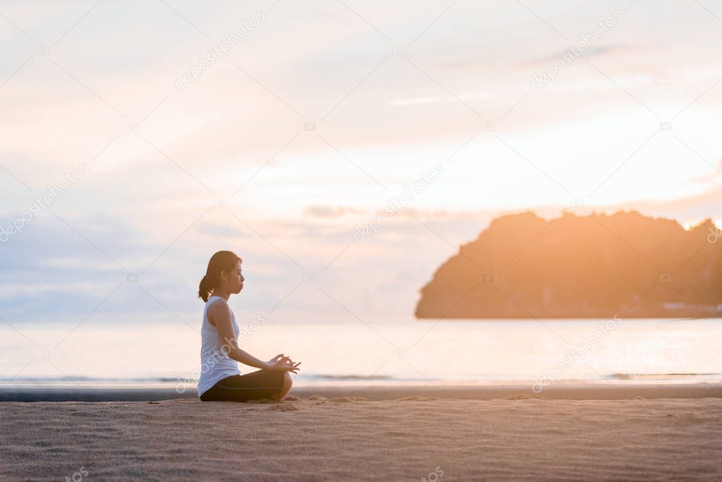 Young woman practicing yoga on the beach at sunset.