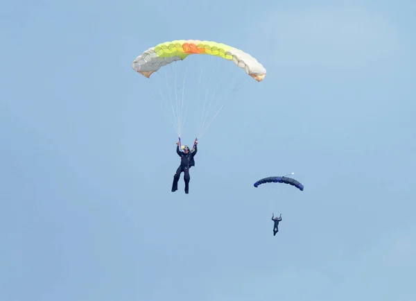 Två fallskärmshoppare med färgglada rännor närmar sig landningsområde i — Stockfoto