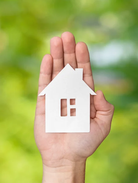 Hand holding white paper house figure on green background — Stock Photo, Image