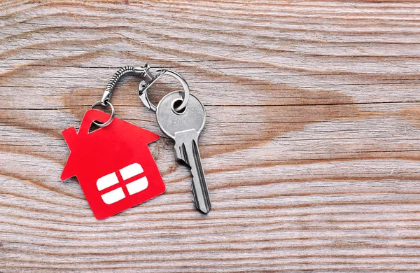 Silver key with red house figure on wooden background Stock Image
