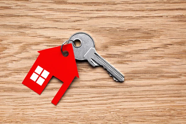 Silver key with red house figure on wooden background Royalty Free Stock Photos