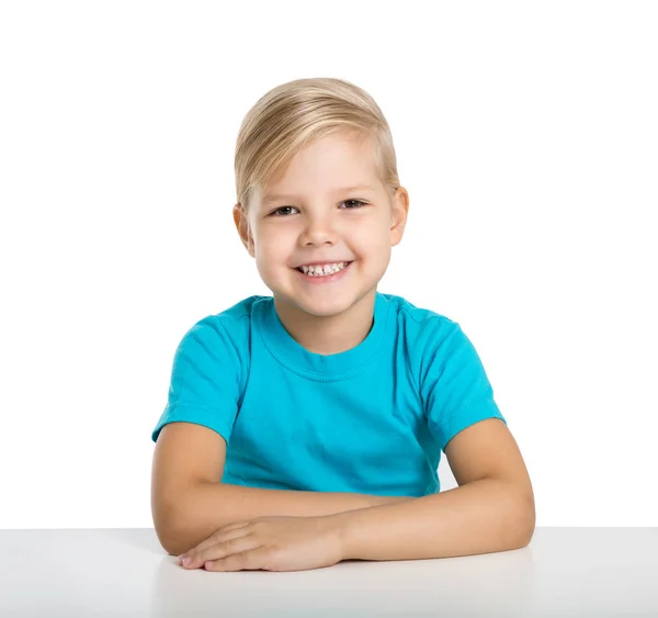 Menina feliz senta-se a uma mesa e sorri Fotos De Bancos De Imagens