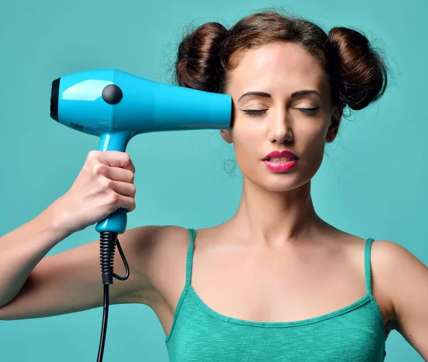 Happy young curly brunette woman with hair dryer on blue mint ba — Stock Photo, Image