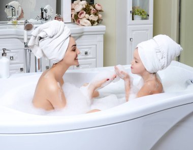 Genç anne ve kızı hu gülümseyerek mutlu bir banyo oynarken