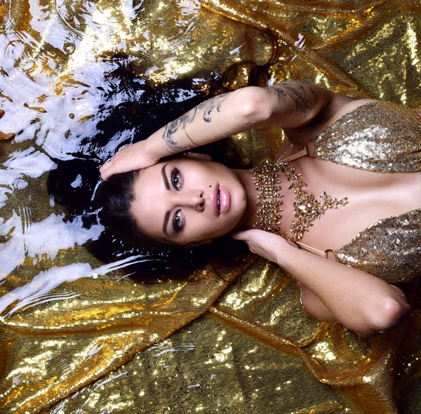 年轻美丽性感的女人躺在金色的水在比基尼下降 — 图库照片