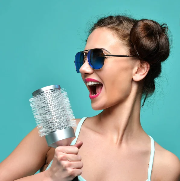 Moda morena mulher cantando com grande escova de cabelo em modernos óculos de sol aviador — Fotografia de Stock