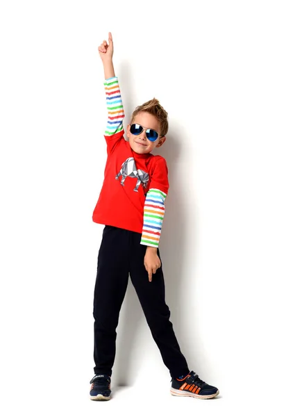 Niño feliz de pie en camisa de color rojo claro apuntando con el dedo hacia arriba en las gafas de sol —  Fotos de Stock