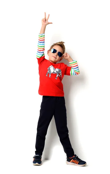 Niño feliz de pie en camisa de color rojo claro mostrando señal de paz con la mano en gafas de sol —  Fotos de Stock