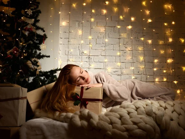 Junge Frau liegt träumend neben magischen Neujahrsgeschenken am Weihnachtsbaum — Stockfoto