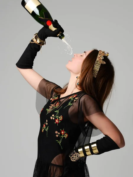 Elegantes mujeres jóvenes sostienen bebida salpicadura botella de champán y oro presente en la corona — Foto de Stock