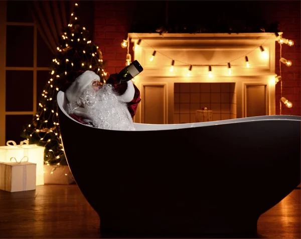Bad Santa Claus lying in bathtub over christmas tree interior background with retro light bulbs drinking champagne alcohol from the bottle — Stock Photo, Image