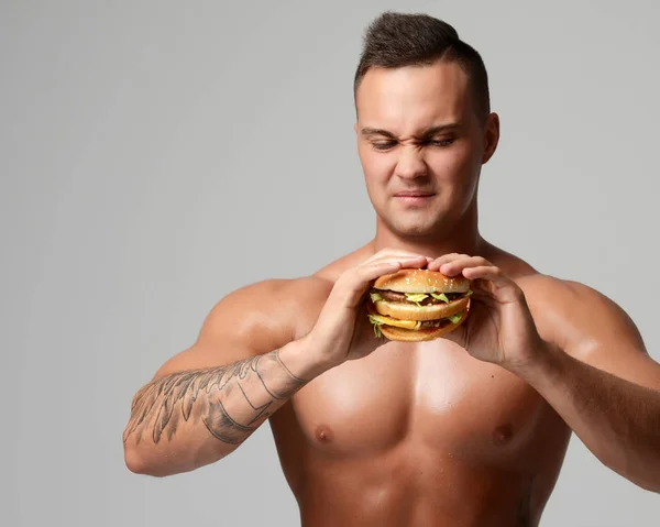 Young strong muscular athlete men look at unhealthy junk fast food burger cheeseburger