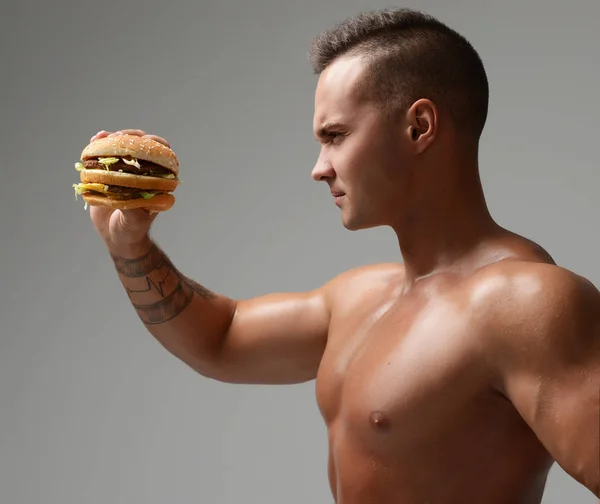 Молодые сильные мускулистые спортсмены смотрят на нездоровый фаст-фуд чизбургер — стоковое фото