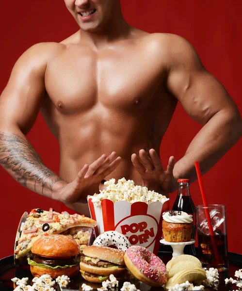 Młody silny lekkoatletka mięśni mężczyzn ciała push powrotem niezdrowe śmieci fast food burger pączek ciasto popcorn pizza — Zdjęcie stockowe