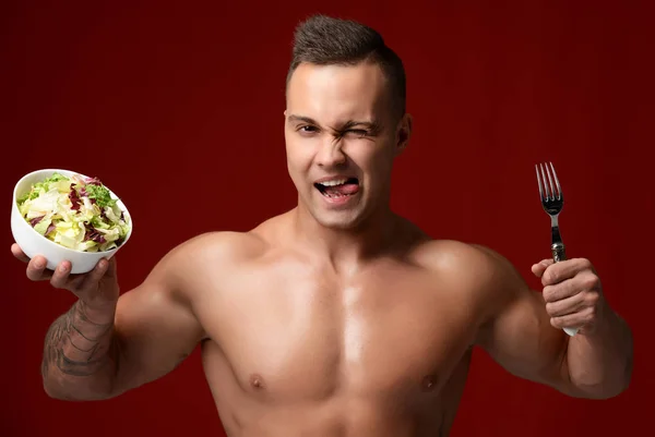Портрет сильного мускулистого спортсмена со свежим салатом и вилочкой, улыбающейся подмигивая — стоковое фото
