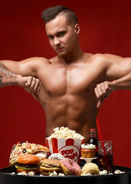 Joven fuerte atleta muscular hombres cuerpo empujar hacia atrás basura insana comida rápida hamburguesa rosquilla pastel palomitas de maíz pizza —  Fotos de Stock