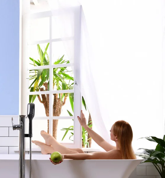 Joven hermosa mujer tumbada en la bañera y tomando baño cerca de la ventana del baño abierto —  Fotos de Stock