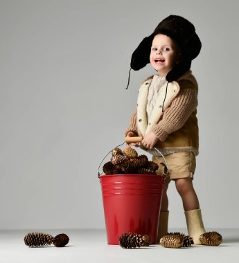 Kış retro şapkalı küçük çocuk çocuk ayağa ve elinde kırmızı Noel kova çam kozalakları tam tutun