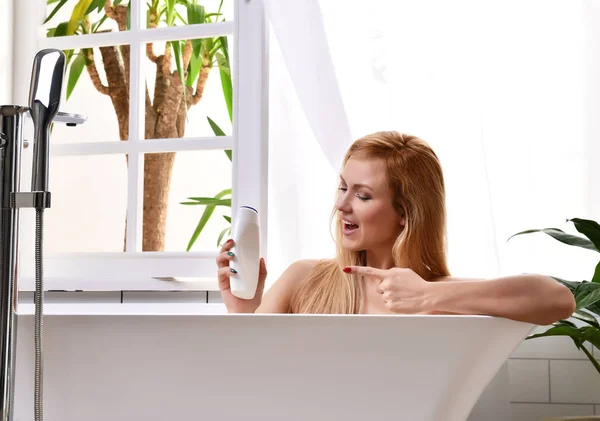 Kvinna i badkar med bad nära öppet badrum fönster och tvätta handen med mjuk dusch gel grädde lotion — Stockfoto