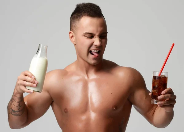 Портрет сильного мускулистого спортсмена держит молоко или кефир по сравнению с содовой — стоковое фото