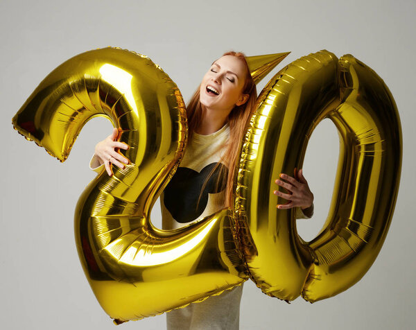 Young happy girl with huge gold digit twenty balloons as a present for birthday 