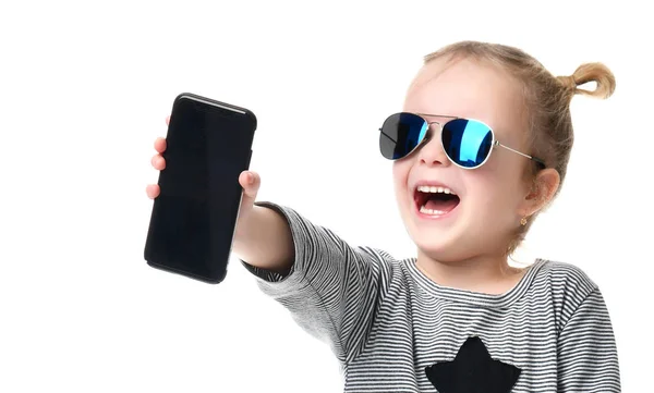 Portrait of a smiling little pretty girl showing blank screen mobile phone in blue sunglasses — Stock Photo, Image