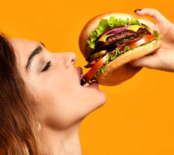 Mujer comer sándwich de hamburguesa con boca hambrienta sobre fondo amarillo — Foto de Stock