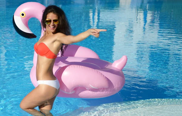 Vrouw in een zwembad recreatie op een gigantische opblaasbare giant roze flamingo float matras in rode bikini — Stockfoto