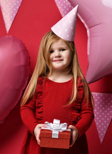 Adorable pretty girl with pink balloons and red present gift and birthday cap — Stock Photo, Image