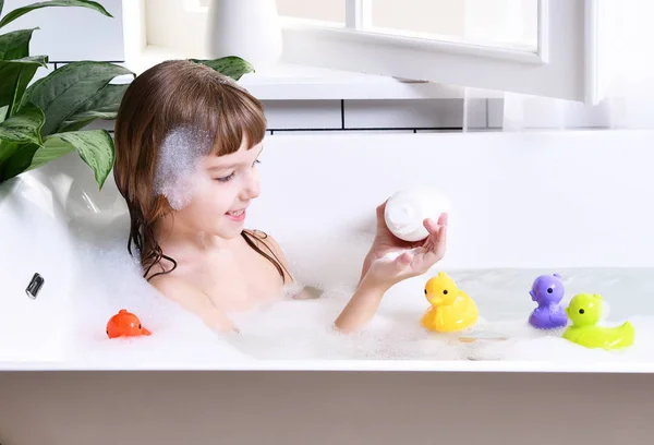 Feliz niña sentada en la bañera jugando con juguetes de pato en el baño —  Fotos de Stock