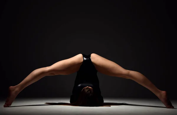 Jovem esporte mulher ginástica fazendo alongamento exercício de fitness no ginásio escuro — Fotografia de Stock