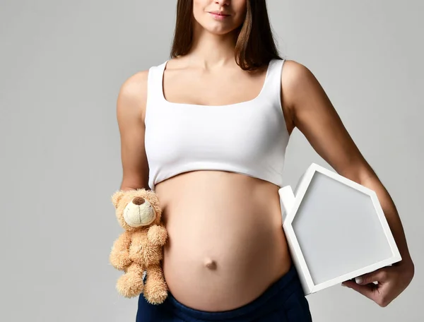 Gravid kvinna i vit topp skjorta håller hus och Nalle — Stockfoto