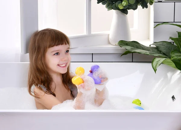 Feliz niña sentada en la bañera jugando con juguetes de pato en el baño —  Fotos de Stock