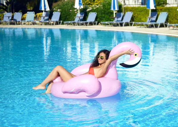 Vrouw in een zwembad recreatie op een gigantische opblaasbare giant roze flamingo float matras in rode bikini — Stockfoto