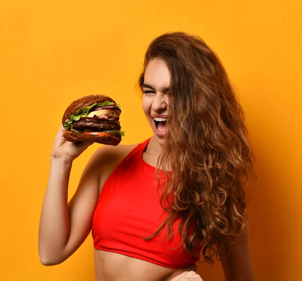 Mulher come sanduíche de hambúrguer com boca faminta no fundo amarelo — Fotografia de Stock