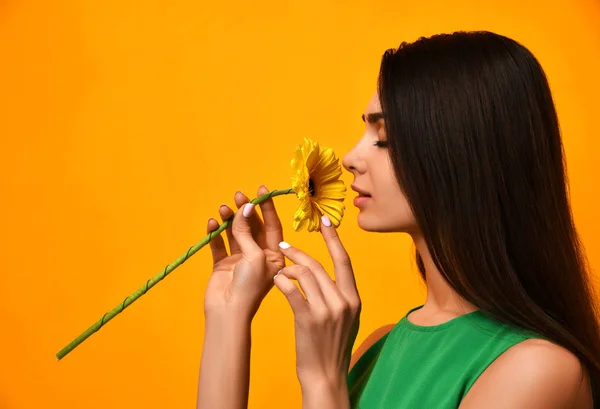Молода красива жінка відчуває запах жовтої квітки гербери в зеленому платті — стокове фото