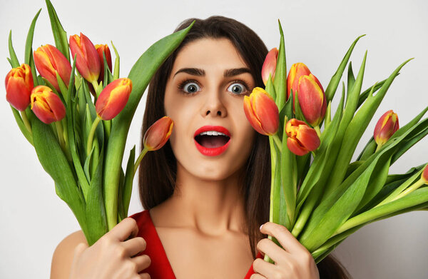 Beautiful woman with bouquet of tulip flowers in red dress surprised.